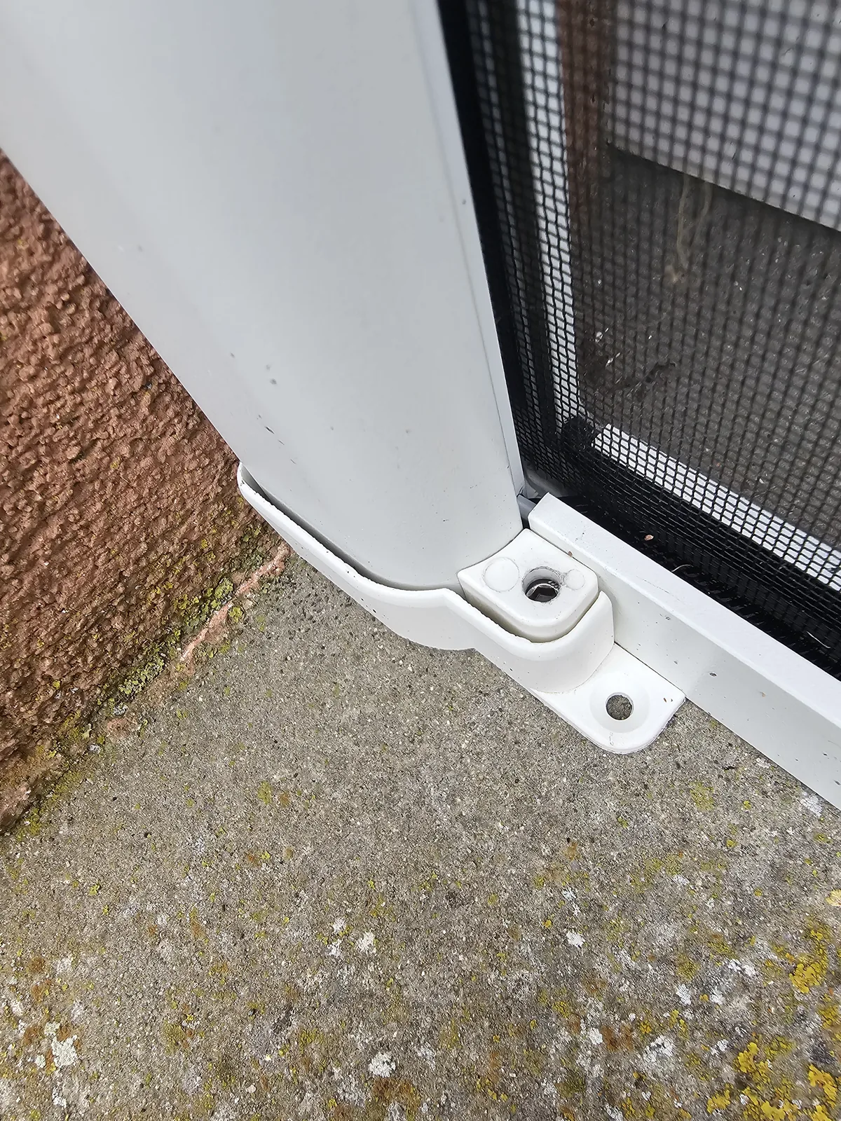 Embout blanc de la moustiquaire coulissante vissé au sol, au départ du rail bas, contre le crépi.