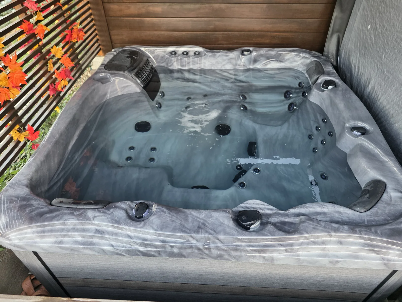 Spa gris marbre installé sur une terrasse en bois, vu de dessus, cuve à jets et cadre bois, brise-vue à lames sur le côté.